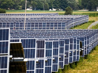 The image depicts rows and rows of solar panels in a 140-acre solar field. 