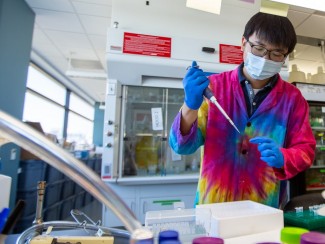 Sae-Byuk Lee stands in front of a lab bench pipetting samples in his tie-dyed lab coat