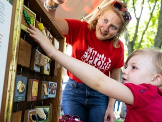 A child reaching to turn a tile in a wooden grid while a smiling adult watches