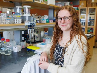 Woman with red hair and glasses poses for a photo in front of a lab bench