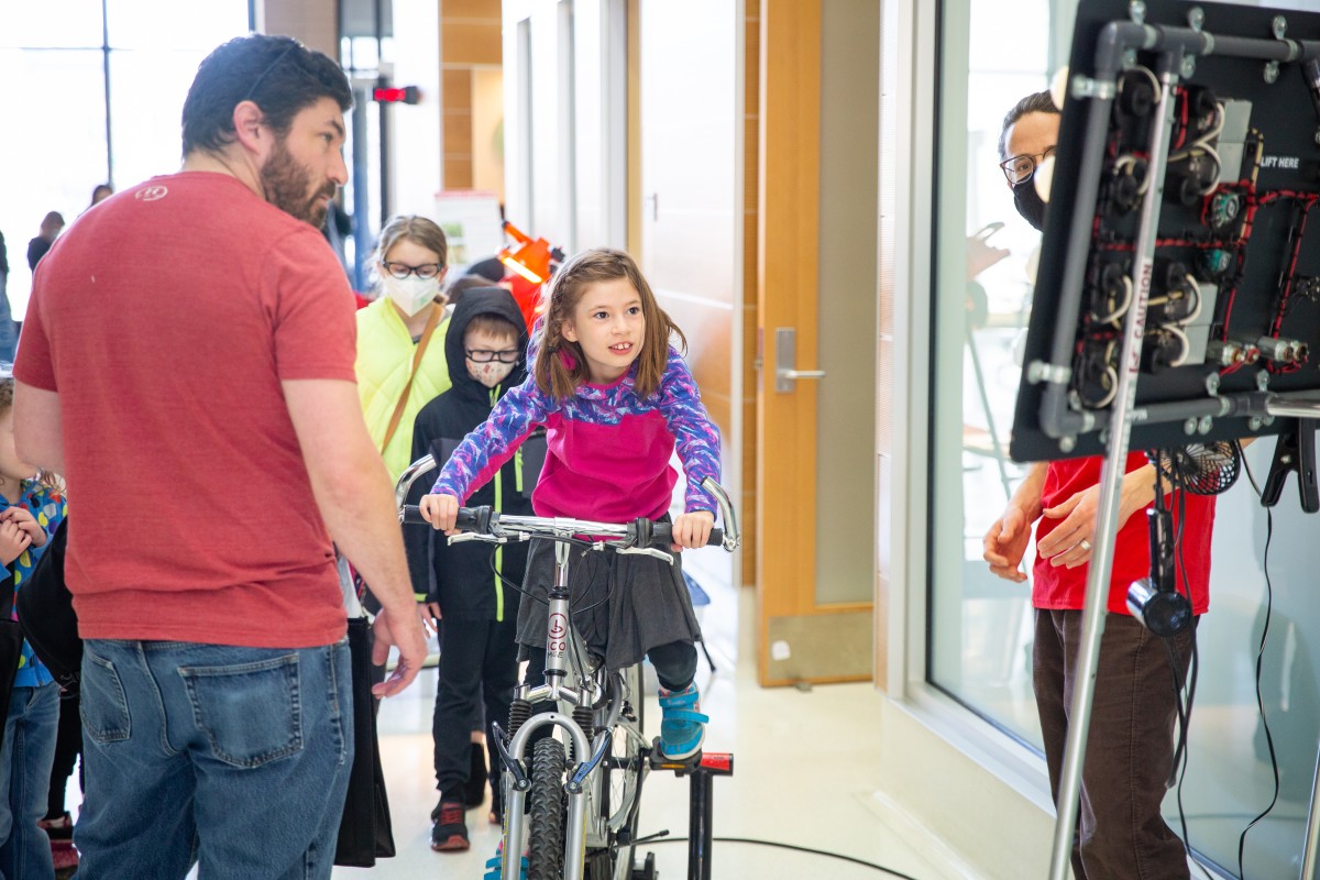 A kid pedals hard on a stationary bike to power lightbulbs.