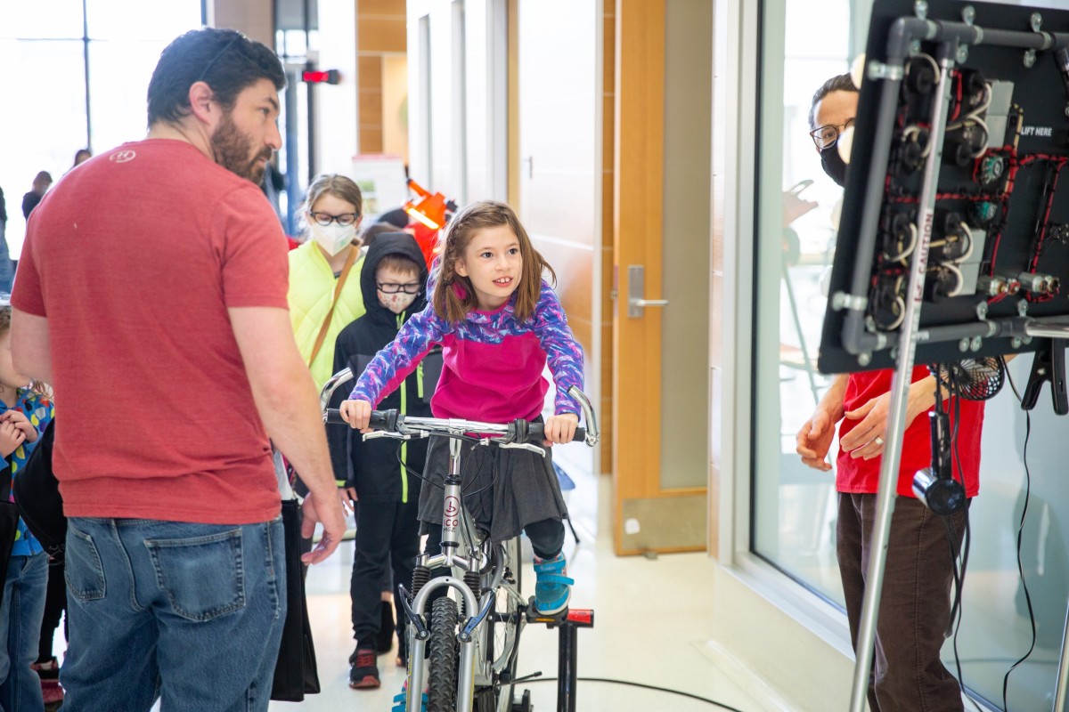 A kid pedals hard on a stationary bike to power lightbulbs.