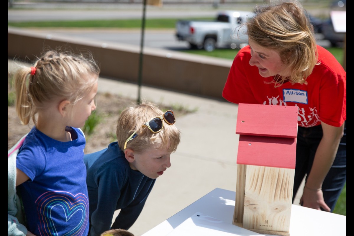 Two children look at the pollinator hotel with a scientist in a red shirt.