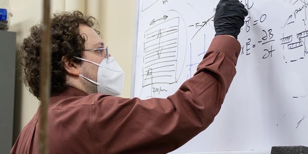 Mikhail Kats writes on a whiteboard in his lab